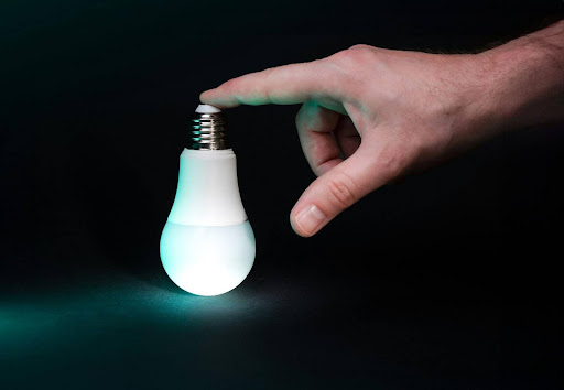 Hand turning on an energy-efficient light bulb representing energy awareness at home