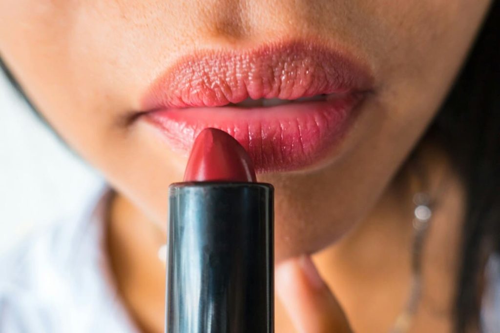 Close-up of lips as a person applies red lipstick from a lipstick tube.